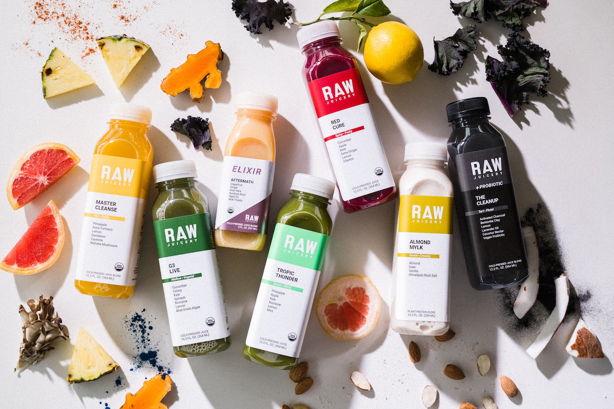 Different Raw Juicery bottles surrounded by various fruits and vegetables