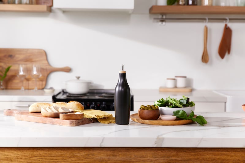 Black olive oil dispenser with bread and salad on kitchen counter