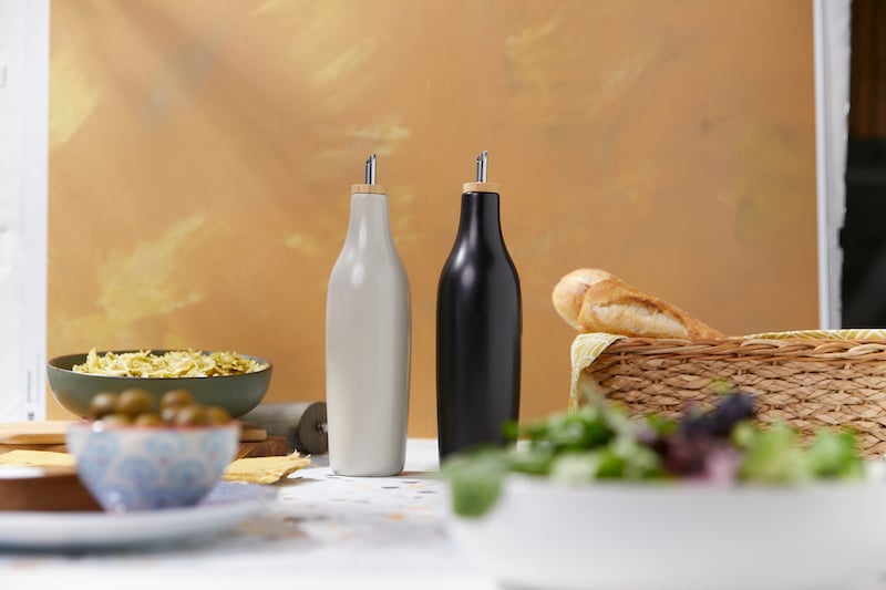 Two olive oil dispensers surrounded by bowls of salads, olives, pasta and bread