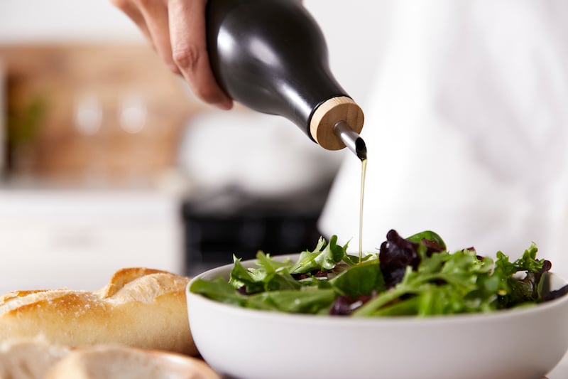 Hand pour olive oil onto salad