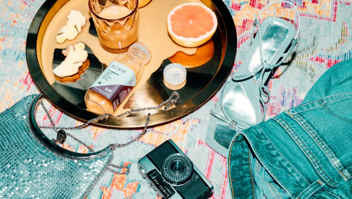 RAW Juicery bottle surrounded by various items like camera, jeans and sequined purse
